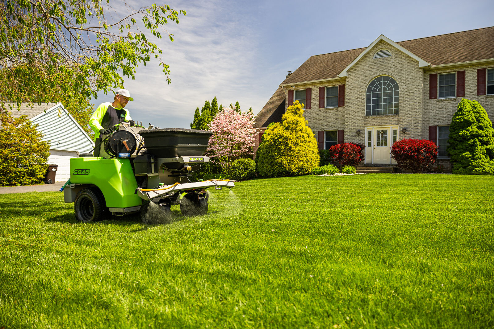 lawn care technician operating a lawn sprayer for weed control in front of a nice house