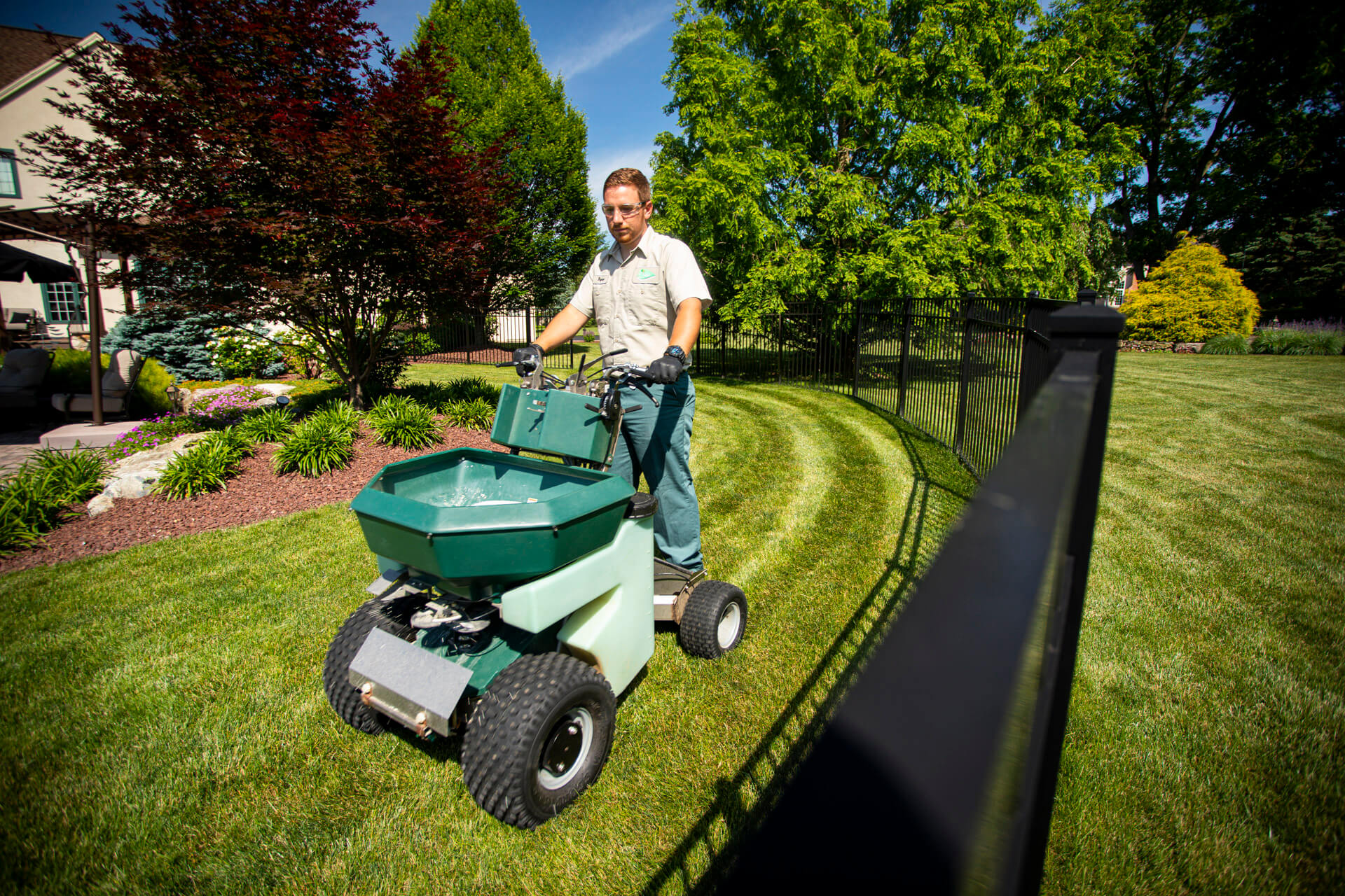 lawn care technician running sprayer on backyard grass